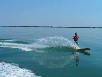 Full length of shirtless man wakeboarding in sea against clear sky