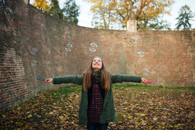 Full length of smiling woman standing in park during autumn