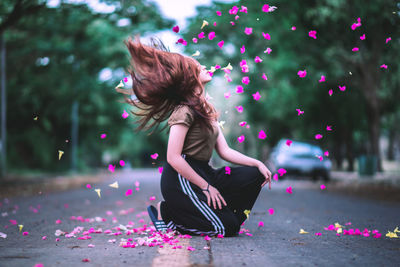 Side view of young woman with petals kneeling on street