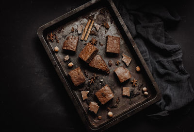 Pieces of baked chocolate brownie pie in a metal baking sheet on a black table, top view