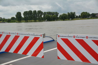 Barricade at boat on river against cloudy sky