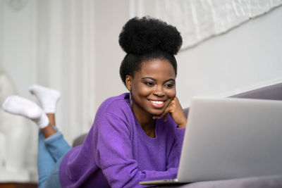 Close-up of smiling woman using laptop sitting on sofa at home