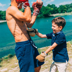 Shirtless grandfather with grandson boxing by swimming pool