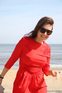 Portrait of happy beautiful woman in red dress at beach against sky