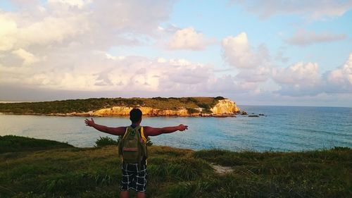 Rear view of man standing on cliff with arms outstretched against sky