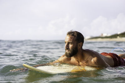 Portrait of shirtless man swimming in sea against sky