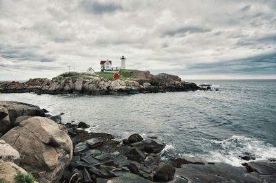 Distant view of lighthouse on shore against cloudy sky