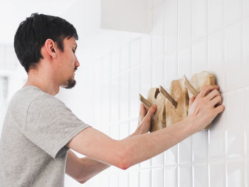 A young man hangs a wooden hanger on the wall in the bathroom.