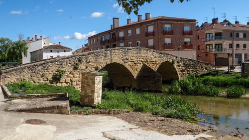 Arch bridge over river by buildings against sky