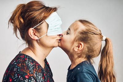 Little girl kissing her mother who has covered eyes with face mask for fun. daughter giving kiss