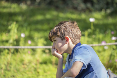 Upset little caucasian boy feels hurt sad bored thoughtful sitting alone in a park.