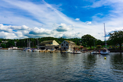 Sailboats in river by buildings against sky