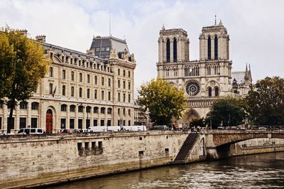 Bridge over river by buildings against sky in city