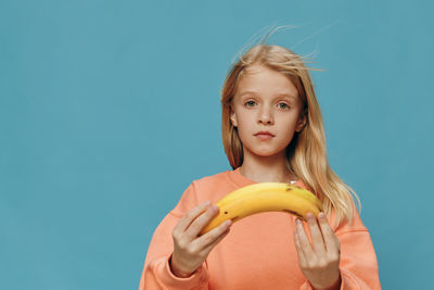 Portrait of young woman holding banana against blue background