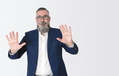 Stylishly dressed bearded hipster in blue jacket on white, raising hands and showing palms,