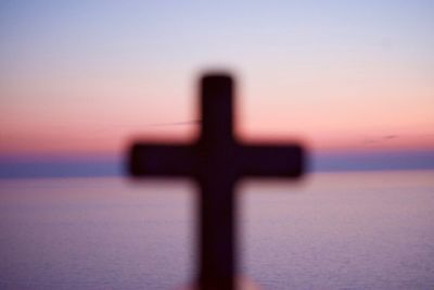 Close-up of silhouette cross on shore against sky during sunset