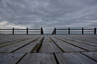 Wooden pier on jetty leading towards sea against sky