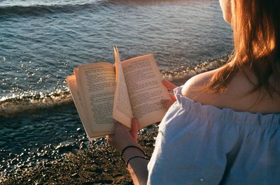 Rear view of woman reading book at beach