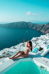 Rear view of woman sitting on sea against sky in santorini