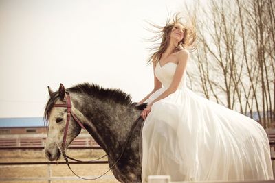 Beautiful bride riding horse on field against sky