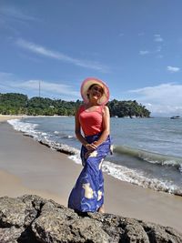 Woman wearing hat standing on rock at beach