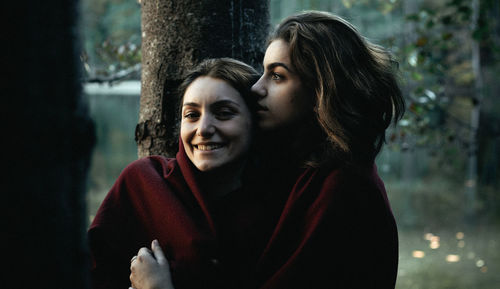 Side view of woman embracing smiling friend in forest