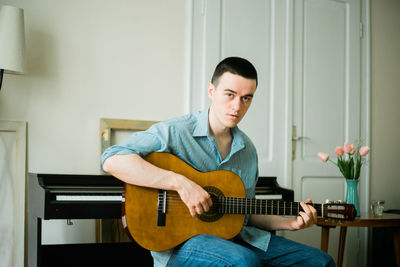 Portrait of young man playing guitar at home