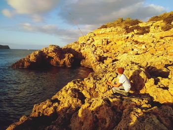Man sitting on rock by sea against sky