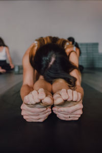 Unrecognizable barefooted female in activewear stretching body while doing paschimottanasana pose sitting on sports mat on floor in modern gym