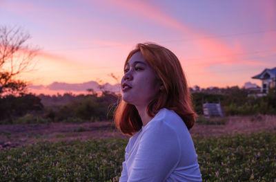 Portrait of young woman sitting on field against sky during sunset