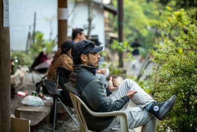 Side view of man gesturing while sitting on chair at yard