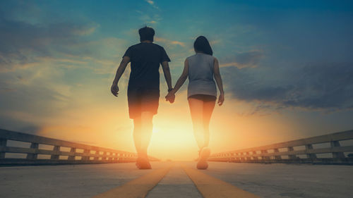 Rear view of women standing on bridge at sunset