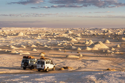 Automobiles parked on sandy ground in white desert national park with abundance of chalk rocky formations during trip in egypt