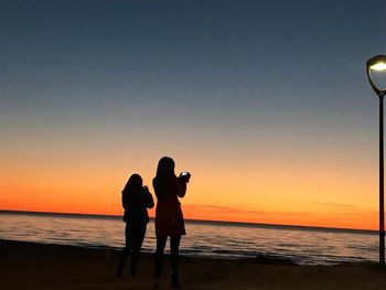 Silhouette women standing on beach against sky during sunset