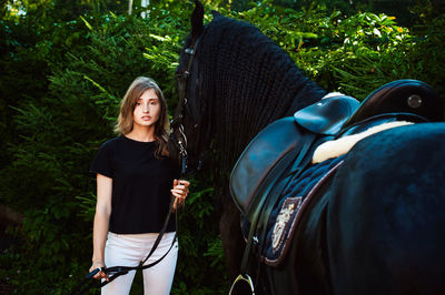 Portrait of young woman standing with horse against trees