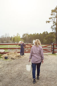 Rear view of female farmer carrying bucket in farm