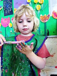 Girl painting hand while standing against wall