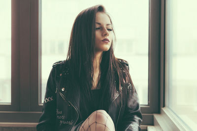 Beautiful young woman looking through window at home