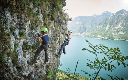 Girl with brother climbing mountain with lake idro in background