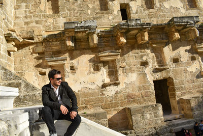 Young man sitting against old building