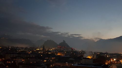 Illuminated buildings in city against sky at sunset