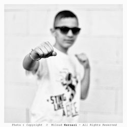 Portrait of young man wearing sunglasses standing against wall