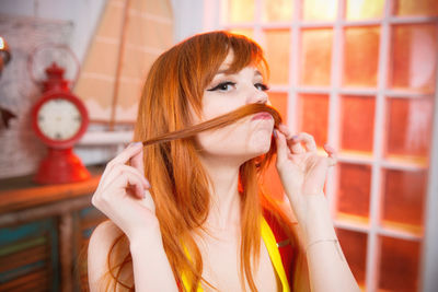 Portrait of beautiful redhead woman making mustache with hair in room
