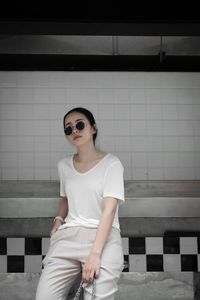 Young woman wearing sunglasses sitting against wall
