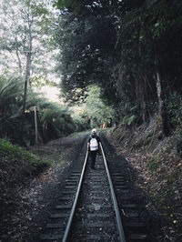Rear view of person walking on railroad track