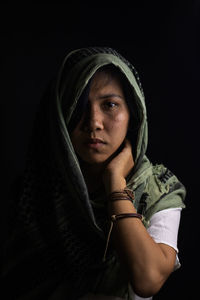 Portrait of young woman covered with scarf against black background