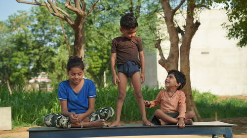 Two indian little girl and a boy doing meditate yoga asana on roll mat with eyes closed in park.