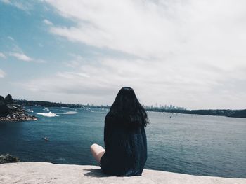 Rear view of woman sitting on rock against sea