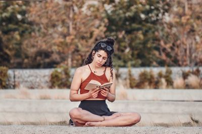 Young woman reading book while sitting on land