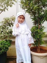 Cute girl standing by potted plant against trees